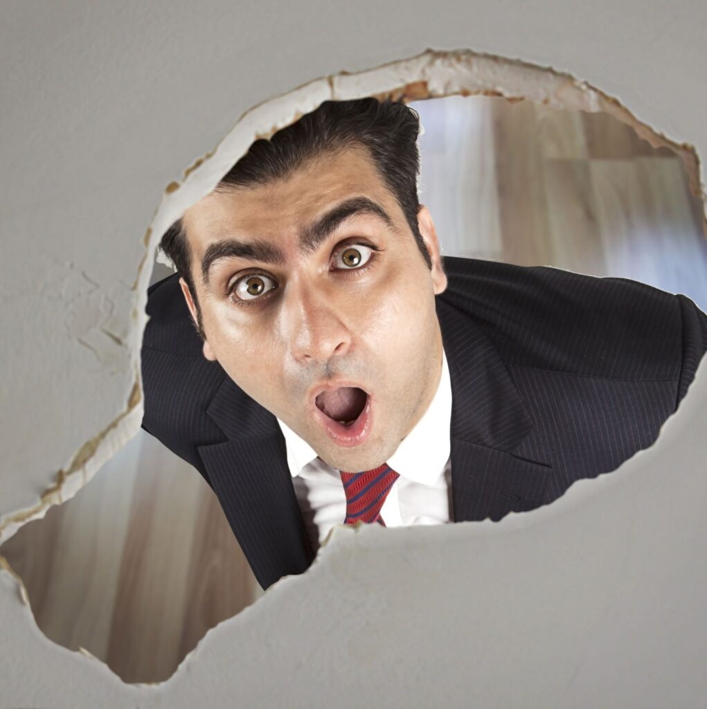 shocked man looking up at roof leak hole in ceiling