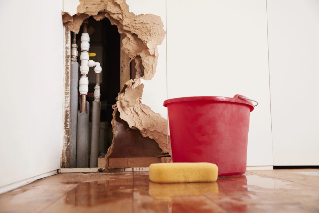 burst pipe in wall with bucket and sponge